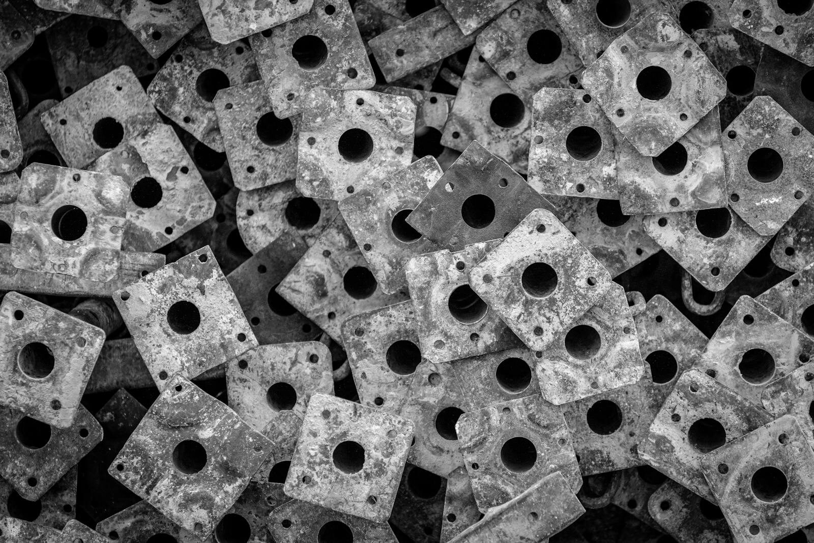 A close-up abstract composition of stacked, perforated metal plates in black and white, showcasing texture and pattern.